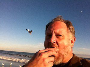 Arik Bjorn eating a doughnut and jealous seagull. Credit: Jaroslav Dampfstain. IMG_3349